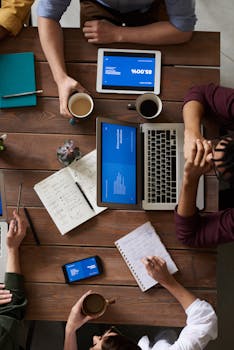 Group of coworkers discussing business strategies with laptops and tablets in a modern office setting.